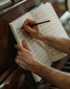 A person composing music with pencil and sheet on a piano. Captures artistic creativity.