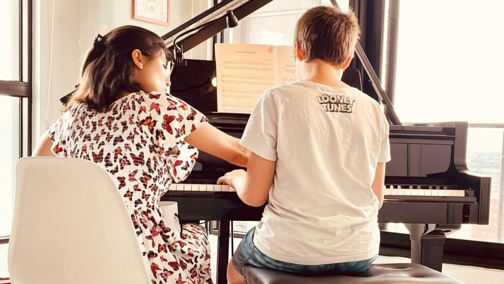A young boy receives a piano lesson from a female instructor in a bright room.