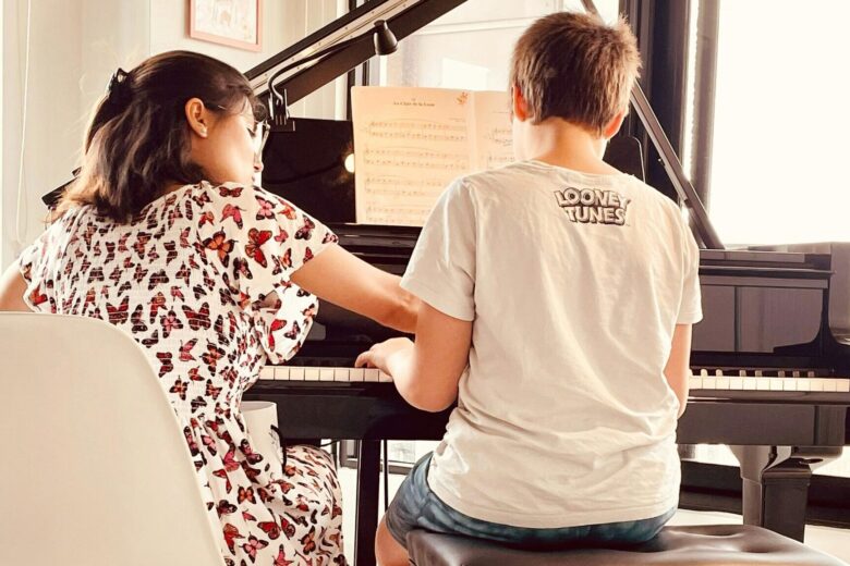 A young boy receives a piano lesson from a female instructor in a bright room.
